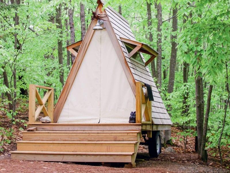 A-frame tiny home on wheels with wooden steps in a forest setting, space-saving design